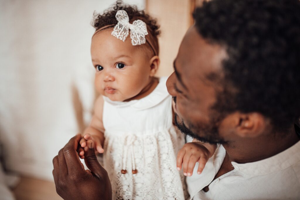 Father holding his baby daughter indoors, symbolizing intentional fatherhood, emotional connection, leadership, and family legacy.