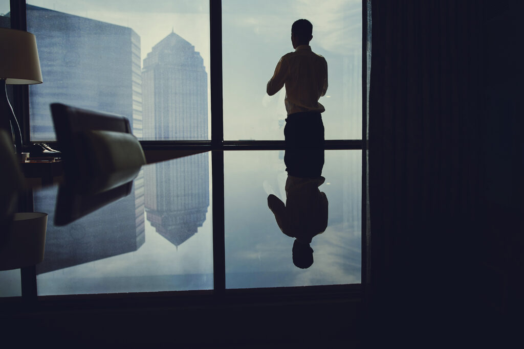 Business leader standing alone by a window overlooking the city, reflecting on leadership identity, values, and decision-making under pressure.