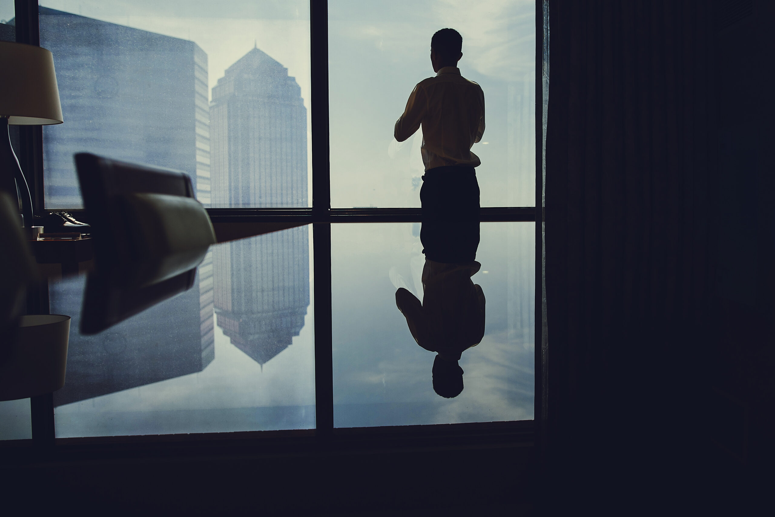Business leader standing alone by a window overlooking the city, reflecting on leadership identity, values, and decision-making under pressure.