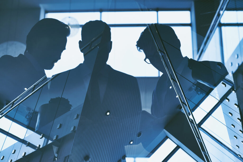Silhouetted executive leaders standing behind glass in a modern office, representing organizational alignment, leadership accountability, and workplace trust.