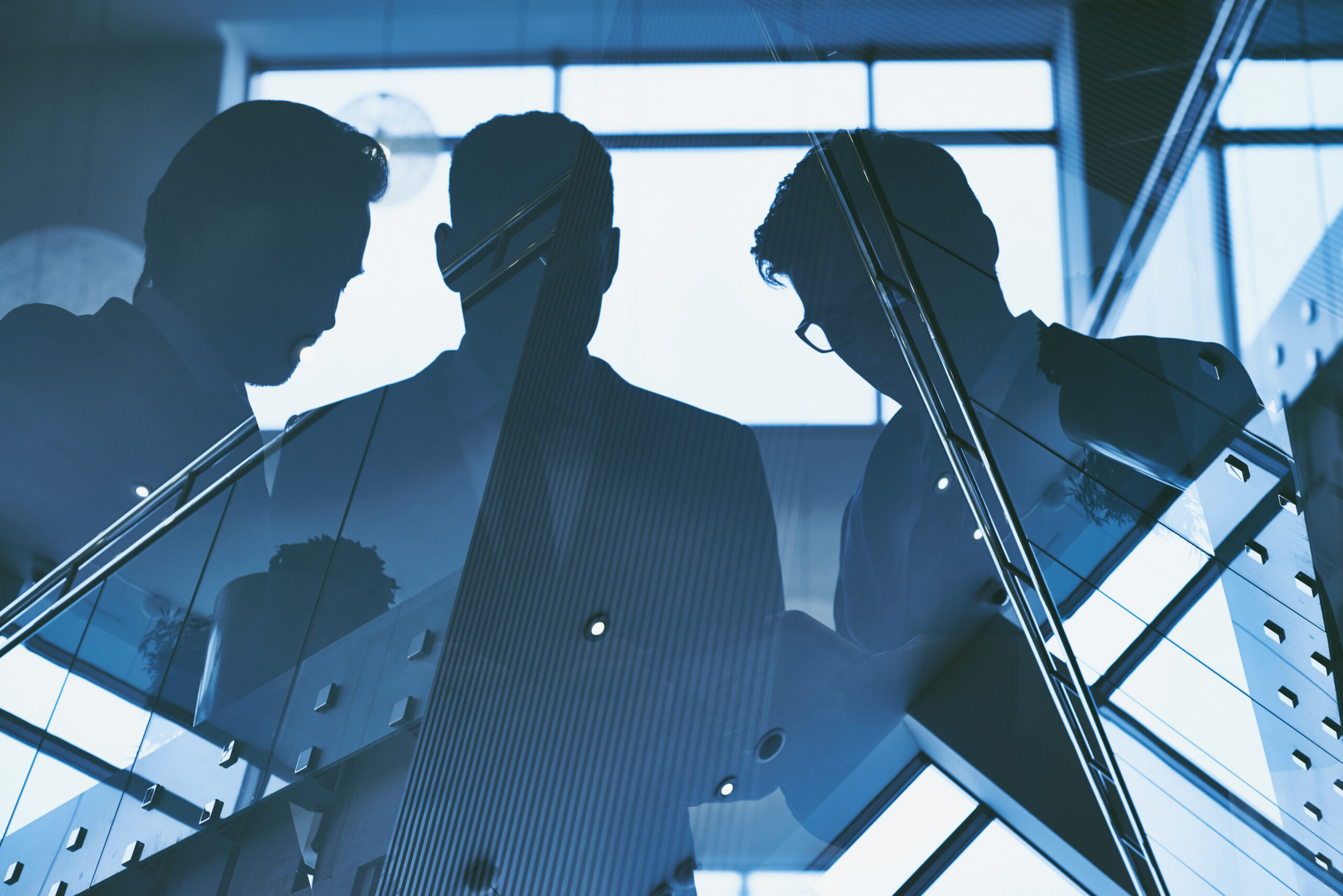 Silhouetted executive leaders standing behind glass in a modern office, representing organizational alignment, leadership accountability, and workplace trust.