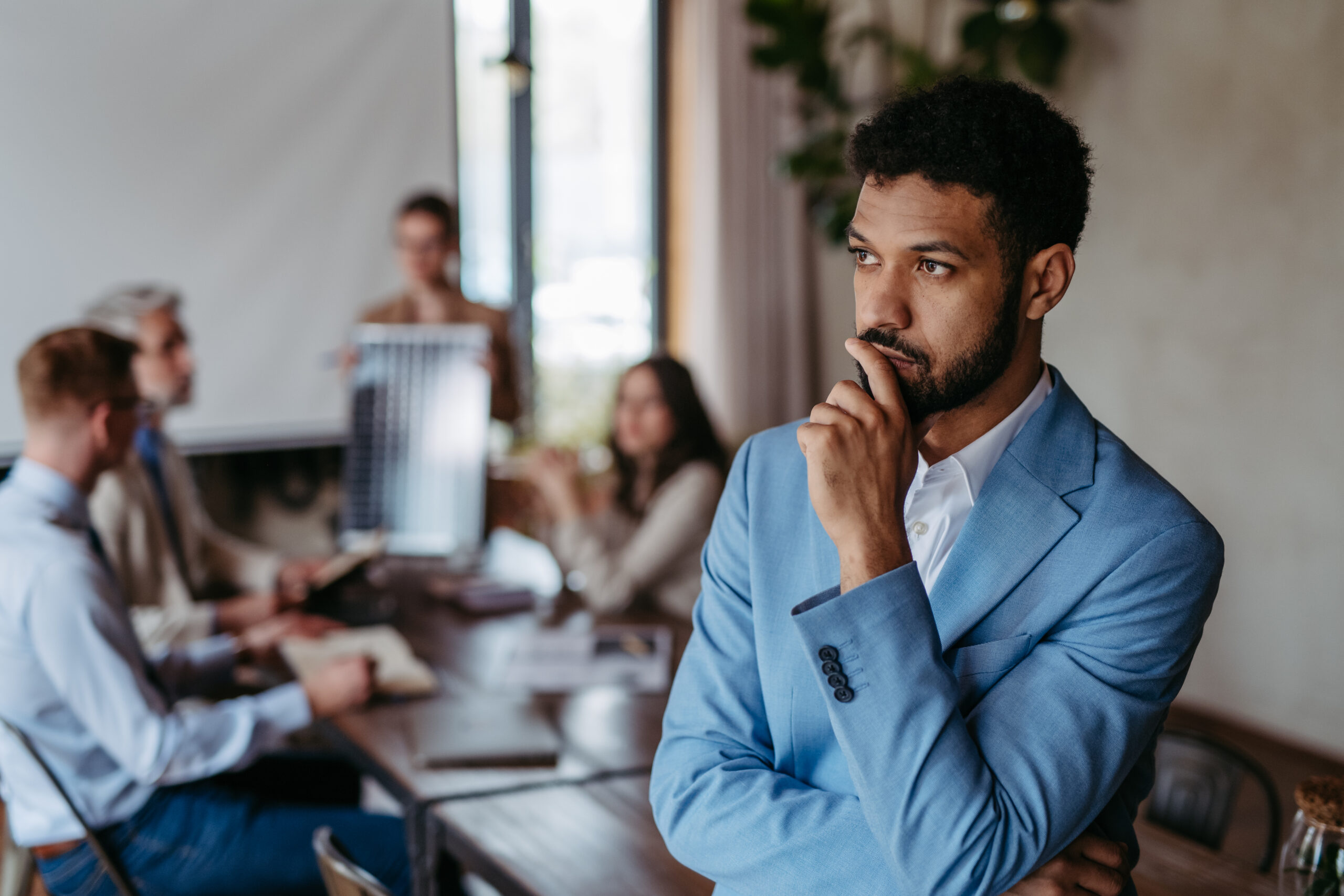 Thoughtful business leader considering a difficult decision while employees meet in the background.
